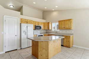 Kitchen featuring appliances with  a center island, light brown cabinetry, light countertops, and light tile patterned floors