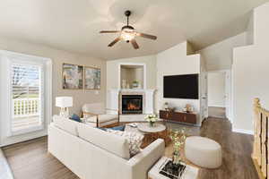 Living room with vaulted ceiling, a tiled fireplace,LVP finished floors, and ceiling fan (virtual staging)