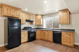 Kitchen featuring new black appliances, light brown cabinets, under cabinet range hood, granite countertops