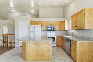 Kitchen with appliances with, light countertops, light tile patterned floors, light brown cabinets, and high vaulted ceiling