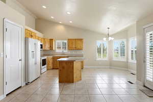 Kitchen with vaulted ceiling, white appliances, hanging lights, a kitchen island, and light countertops