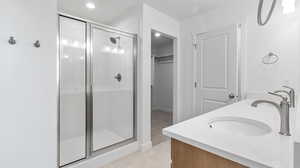 Bathroom featuring double vanity, a spacious closet, a stall shower, light tile patterned flooring, and recessed lighting