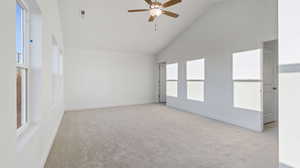 Spare room with light carpet, high vaulted ceiling, ceiling fan, and plenty of natural light