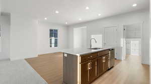 Kitchen featuring a center island with sink, recessed lighting, light wood-type flooring, stainless steel dishwasher, and dark brown cabinets