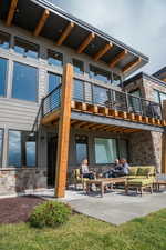 Rear view of property featuring stone siding, a patio, and a balcony