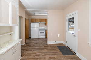 Kitchen with white appliances, dark wood-style floors, tile countertops, under cabinet range hood, and brown cabinetry