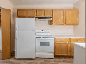 Kitchen featuring white appliances, light countertops, under cabinet range hood, light wood-style flooring, and open shelves