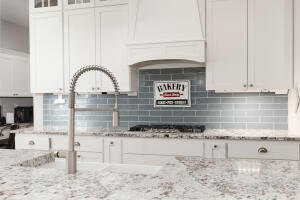 Kitchen featuring light stone counters, white cabinetry, backsplash, and custom range hood