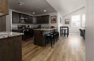 Kitchen with lofted ceiling, a kitchen breakfast bar, appliances with stainless steel finishes, dark brown cabinets, and recessed lighting