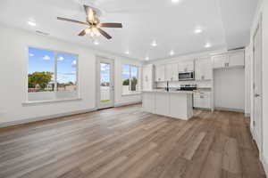 Kitchen featuring an island with sink, white cabinets, light wood-style flooring, light stone countertops, and open floor plan