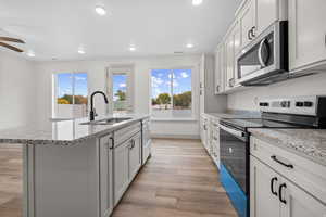 Kitchen featuring stainless steel appliances, light stone countertops, light wood-style flooring, an island with sink, and healthy amount of natural light