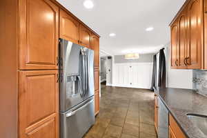 Kitchen with stainless steel appliances, brown cabinetry, a wainscoted wall, recessed lighting, and dark stone counters