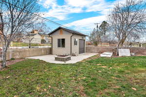 Rear view of property featuring a patio, a fenced backyard, an outbuilding, and an outdoor fire pit