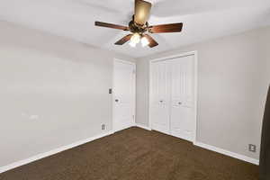 Unfurnished bedroom with dark carpet, a closet, and a ceiling fan