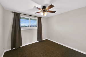 Empty room featuring dark carpet and ceiling fan