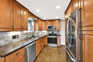Kitchen with stainless steel appliances, brown cabinets, dark stone countertops, backsplash, and recessed lighting