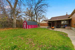 View of green lawn featuring a shed, a patio area, and an outdoor fire pit
