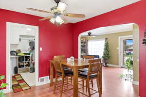 Dining room with light wood finished floors, arched walkways, and ceiling fan