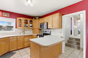Kitchen featuring glass insert cabinets, light countertops, appliances with stainless steel finishes, a peninsula, and light tile patterned floors