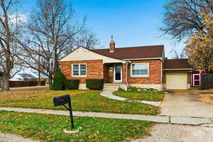View of front of house featuring brick siding, a chimney, driveway, and a shingled roof