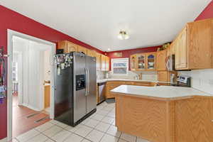 Kitchen featuring appliances with stainless steel finishes, light countertops, glass insert cabinets, a peninsula, and light tile patterned flooring