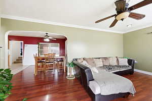 Living area featuring ceiling fan, arched walkways, dark wood finished floors, and crown molding