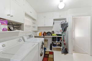 Laundry room featuring light flooring, cabinet space, washer and dryer, and a textured ceiling