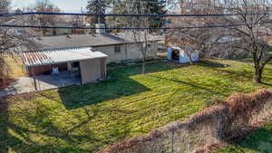 View of grassy yard featuring a patio, a storage shed, concrete driveway, and a carport