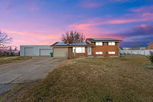Tri-level home with a front yard, roof mounted solar panels, a chimney, a detached garage, and brick siding