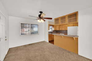 Kitchen featuring light countertops, a ceiling fan, a kitchen breakfast bar, dark colored carpet, and glass insert cabinets