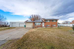 Tri-level home featuring roof mounted solar panels, a chimney, a detached garage, and brick siding