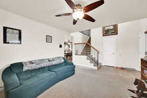 Living room featuring ceiling fan, tile patterned floors, carpet floors, and stairway
