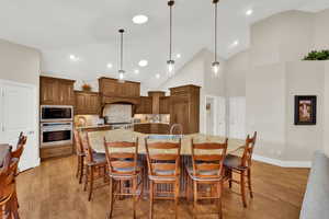 Kitchen with high vaulted ceiling, brown cabinets, a kitchen bar, and pendant lighting