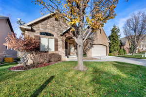View of front facade with driveway, a front yard, stone siding, and a garage