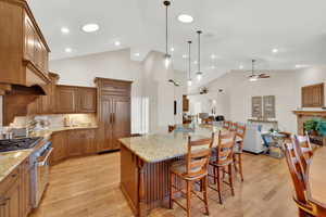 Kitchen featuring high vaulted ceiling, brown cabinets, high end stainless steel range oven, light stone counters, and light wood finished floors