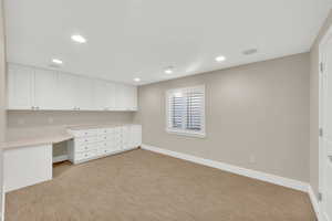 Unfurnished office featuring built in desk, recessed lighting, and light colored carpet