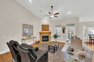 Living room featuring a fireplace, wood finished floors, ceiling fan, vaulted ceiling, and recessed lighting