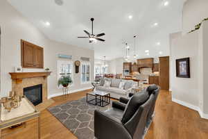 Living room featuring a tile fireplace, a ceiling fan, light wood-type flooring, recessed lighting, and a chandelier