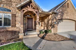 Entrance to property with brick siding, covered porch, driveway, stone siding, and a garage