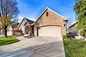 View of front facade with brick siding, a front lawn, driveway, and a garage