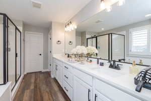Bathroom featuring double vanity, a shower stall, and dark wood-type flooring