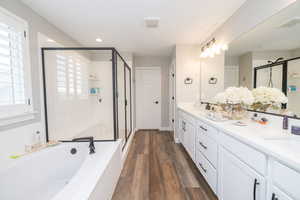 Bathroom featuring a garden tub, double vanity, a stall shower, dark wood-style floors, and recessed lighting