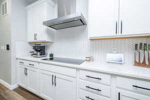 Kitchen with wall chimney exhaust hood, white cabinetry, light stone countertops, black electric stovetop, and dark wood-type flooring
