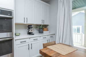 Kitchen featuring stainless steel double oven, white cabinetry, light stone countertops, and wood finished floors