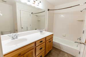 Full bathroom with shower / tub combination, double vanity, and dark tile patterned flooring adjacent to the walk-in closet