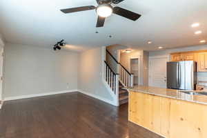 Kitchen with light brown cabinetry, light stone countertops, dark wood-style flooring, and open floor plan