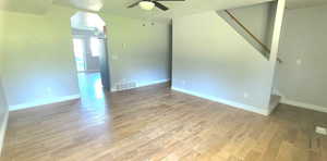 Unfurnished room with a ceiling fan, wood finished floors, arched walkways, and stairway