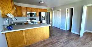 Kitchen with a peninsula, brown cabinets, appliances with stainless steel finishes, dark wood-style floors, and light countertops
