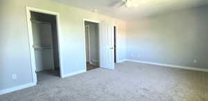 Unfurnished bedroom featuring light carpet, a walk in closet, and a ceiling fan