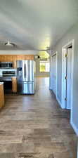Kitchen featuring a textured ceiling, stainless steel appliances, wood finish floors, light countertops, and brown cabinets
